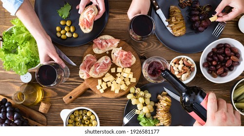 Friends Or Family Are Having Dinner Bruschetta With Ham, Cheese, Baked Potatoes, Olives And Olives With Wine. Snack Dinner Table Concept Top View