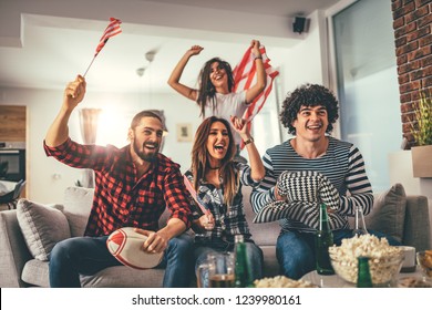 Friends Are Fans Of Sports Games As American Football Love Spending Their Free Time At Home Together. They Are Screaming And Gesturing For A Victory. 