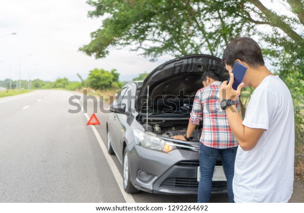 Friends fixing car broken down on highway 
calling for help on mobile phone. Two man friends talking on phone
with assistance  for breakdown car problem.
Broken car on highway
road trip with friends.
