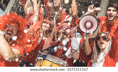 Friends football supporter fans cheering with confetti watching soccer match event at stadium - Young people group with red t-shirts having excited fun on sport world championship concept