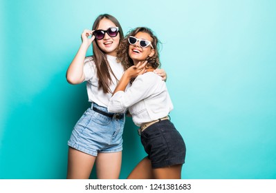 Friends Forever. Two Cute Lovely Girl Friends In Sunglasses Posing With Smile On Blue Background
