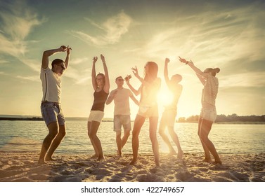 Friends Funny Dance On The Beach Under Sunset Sunlight.