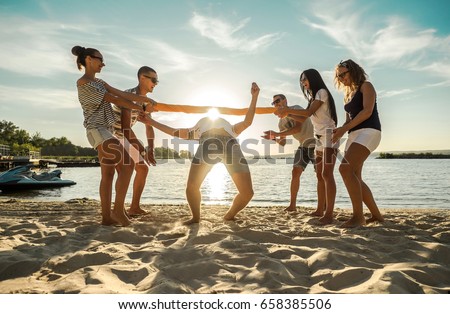 Friends funny game on the beach under sunny sky with clouds at summer day.