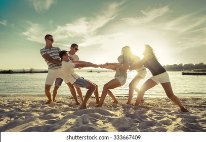 Friends funny tug of war on the beach under sunset sunlight. - Powered by Shutterstock
