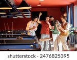 Friends are gathered around a pool table, laughing and enjoying a casual game of billiards in a bar setting.