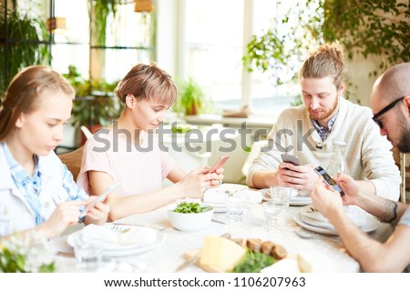 Friends gathering and using smartphone while waiting for order at restaurant