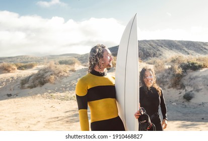 Friends getting ready to go surfing in the sea- People wearing wetsuits to go into the water - Two friends walking on the beach - Powered by Shutterstock