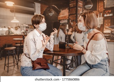 Friends girls met in a cafe and communicate with each other and chat. Wear medical protective masks. An outbreak of the coronavirus epidemic. New rules for social distance and isolation
