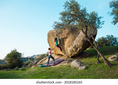 Friends go in for sports in nature, bouldering on rocks, girl climbs a big stone, woman is belayng partner, outdoor recreation, bouldering on the boulders of Lake Bafa