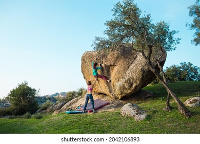 Friends go in for sports in nature, bouldering on rocks, girl climbs a big stone, woman is belayng partner, outdoor recreation, bouldering on the boulders of Lake Bafa