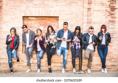 Friends group using smartphone against wall at university college backyard break - Young people addicted by mobile smart phone - Technology concept with always connected milenials - Warm filter image
