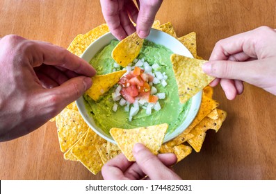 Friends' Hands Eating A Delicious Homemade Guacamole Dip With Nachos