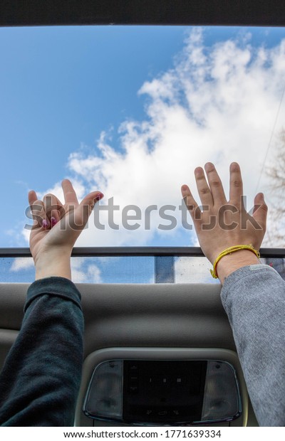 Friends Hands reaching toward the sky through the\
sunroof of a car