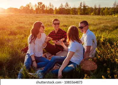 Friends Hanging Out And Eating Pizza Outside. Women And Men Having Picnic At Sunset. Guys Having Fun.