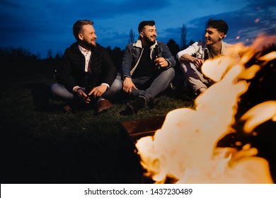 Friends hanging out near the flaming barbecue grill at the sunset