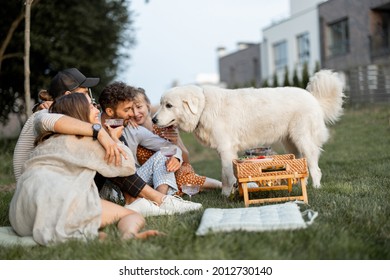 Friends Have Fun Sitting Together With A Huge Dog At Picnic On The Backyard. On The Evening Spending Summer Time In A Small Group Outdoors