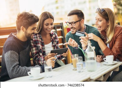 Friends having a coffee together. Two women and two men at cafe shopping on line with digital tablet