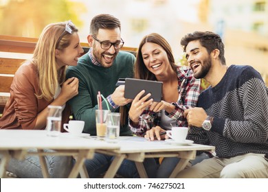 Friends having a coffee together. Two women and two men at cafe shopping on line with digital tablet - Powered by Shutterstock