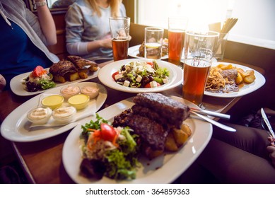 Friends Having A Dinner In The Restaurant With Salad, Barbeque And Beer