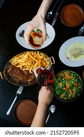 Friends Having Dinner Together. Top View Of Two People Sharing Food At A Dark Table.