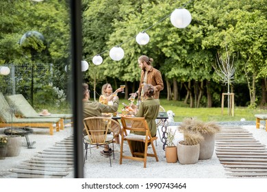 Friends Having A Festive Dinner, Gathering Together At Backyard Of The House In Nature. View Through The Window From The Inside