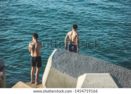 Friends having fun by the sea in summer day, looking at the horizon and preparing to jump off the rocks in the Mediterranean sea. Tense friends before the jump in search of fun.