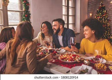 Friends having fun celebrating Christmas, sitting at table, eating, drinking wine and having fun while spending time together during winter holidays