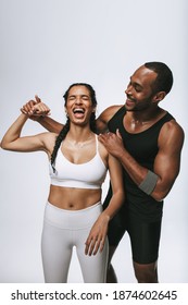 Friends Having Fun At The Gym. Happy Woman In Fitness Wear Showing Her Biceps With Her Male Friend By Her Side.