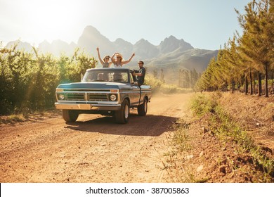 Friends Having Fun In The Open Back Of A Vintage Truck On A Summer Day In Countryside. Young Men And Woman Enjoying On A Road Trip.