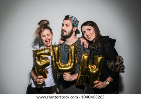 friends having fun, posing and smiling to camera at a white wall having golden letters in hands, playing and fooling around