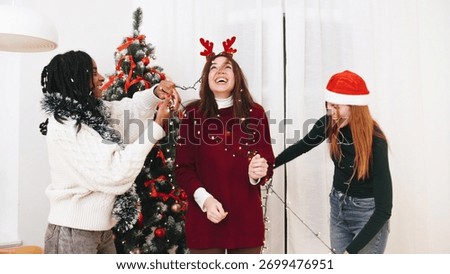 Friends are having fun while decorating a Christmas tree with garlands and lights. They are dressed festively and enjoy each other's company during the holiday season.