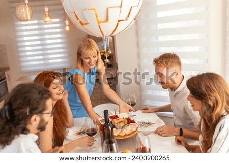 Friends having fun while having dinner party all together at home, hostess serving food and entertaining guests