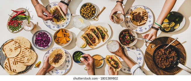 Freunde, die mexikanisches Taco-Abendessen haben. Flaches Legen von Rind-Tacos, Tomatensalsa, Tortillas, Bier, Snacks und Völker Hände über weißem Tisch, Draufsicht. mexikanische Küche, Zusammenkunft, Fest, Komfort-Food-Konzept