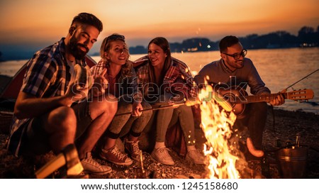 Friends having picnic around the fire.Group of young friends having picnic at night.