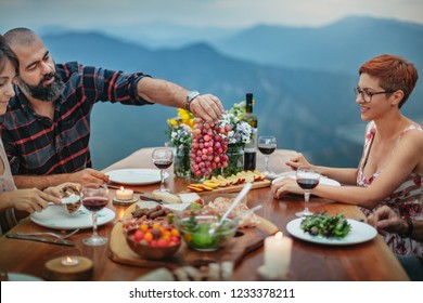 Friends Having Wine And Dinner On A Table Outside In Nature