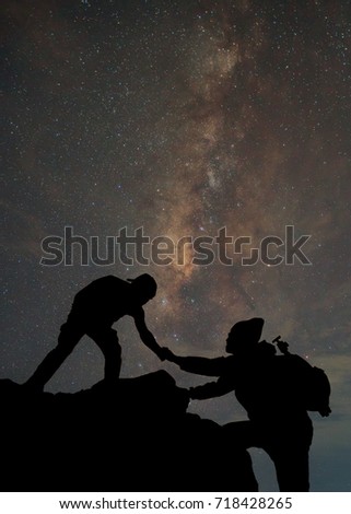 friends helping each other and with teamwork trying to reach the top of the mountains during wonderful the milky way background, Thailand.