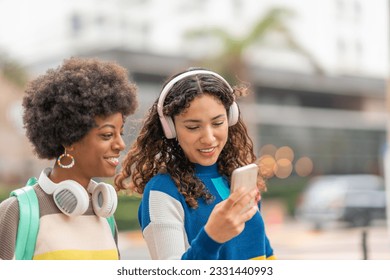 Friends looking at a cell phone and listening to music while walking on the street, with their backpacks on their backs. - Powered by Shutterstock