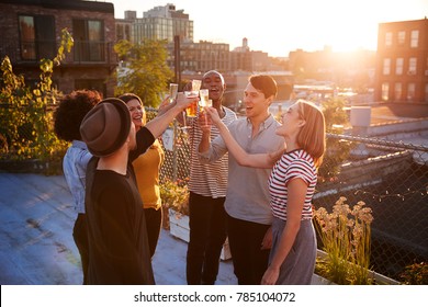 Friends make a toast at a rooftop party, backlit by sunlight - Shutterstock ID 785104072