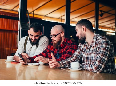 Friends of a man are resting in a cafe , looking in the phone and discussing what they see