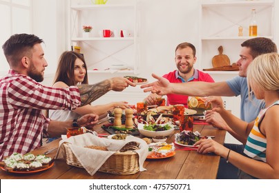 Friends Meeting. Group Of Happy People Talking, Eating, Passing Healthy Meals At Party Dinner Table In Cafe, Restaurant. Young Company Celebrate With Alcohol And Food At Wooden Table Indoors.