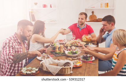 Friends Meeting. Group Of Happy People Talking, Eating, Passing Healthy Meals At Party Dinner Table In Cafe, Restaurant. Young Company Celebrate With Alcohol And Food At Wooden Table Indoors.