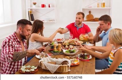 Friends Meeting. Group Of Happy People Talking, Eating, Passing Healthy Meals At Party Dinner Table In Cafe, Restaurant. Young Company Celebrate With Alcohol And Food At Wooden Table Indoors.