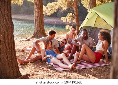 Friends On A Camping Trip Relaxing On A Blanket By A Lake