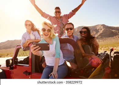 Friends On Road Trip In Convertible Car Taking Selfie