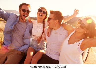 Friends On Road Trip Sitting On Hood Of Convertible Car