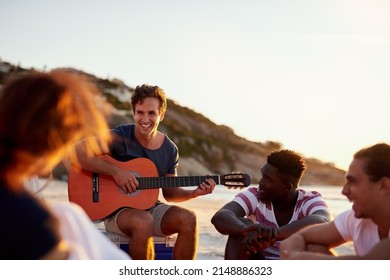 Friends are the ones who inspire and motivate us. Shot of a man playing the guitar while sitting on the beach with his friends. - Powered by Shutterstock