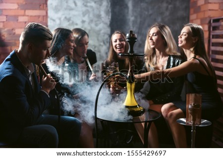 Friends party in hookah lounge. Group of people women and men smoking shisha in cafe or bar, having fun, smiling. Relax concept. Friendship