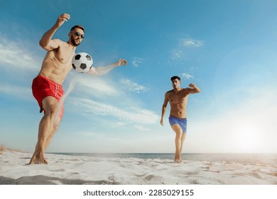 Friends playing football on beach during sunny day, low angle view - Powered by Shutterstock