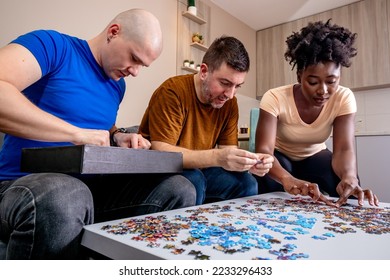Friends playing with jigsaw puzzle at home, on a white wooden table. Putting things together and solving problems. Fun and diversity in friendship. - Shutterstock ID 2233296433