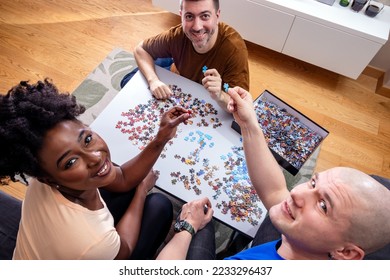 Friends playing with jigsaw puzzle at home, on a white wooden table. Putting things together and solving problems. Fun and diversity in friendship. High Angle View. - Shutterstock ID 2233296437